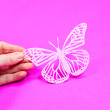 White butterfly cutout held by a hand against a pink background