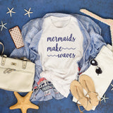 White t-shirt with 'mermaids make waves' text on a blue surface with accessories.