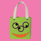 Green tote bag with monster face design on a pink background