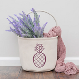Canvas bucket with lavender and a pink blanket on a wooden floor.