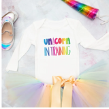 White shirt with 'Unicorn in Training' text, rainbow tutu, and shoes on a light background