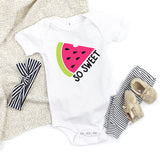 Baby onesie with watermelon design and accessories on a textured surface